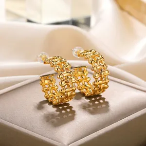 Macro shot of gold-plated C-shaped earrings with intricate woven mesh texture on velvet