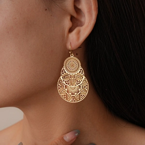 Gros plan de boucles d'oreilles fleur évidée dorées avec détails bohèmes en filigrane