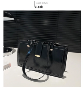 Detail of glossy black shoulder bag with gold hardware on a minimalist desk