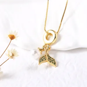 Gold plated fish tail pendant necklace with green stones and pearl on white background