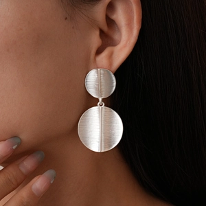 Detailed view of matte brushed silver geometric disk drop earrings on model