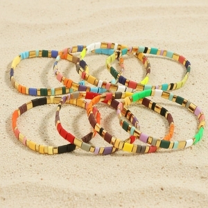 Bohemian colorful Tila bead bracelets with gold accents on beach sand background
