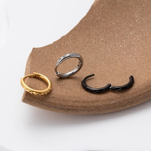 Three engraved stainless steel hoop earrings in gold, silver and black on clay