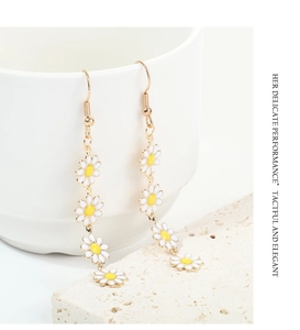 Elegant gold drop earrings featuring white daisy enamel flowers hanging on a ceramic cup