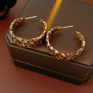 Macro detail of tortoiseshell C-shape resin earrings on a textured jewelry box