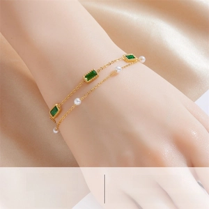 Detail of layered gold chain bracelet with emerald green stones and white pearls on silk
