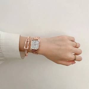 Detail of rose gold square watch with matching bracelet and minimalist rings on wrist