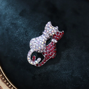 Close-up of a double cat brooch with sparkling red and white rhinestones on velvet
