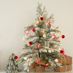 Mini snowy Christmas tree with warm LED lights, red pom-poms, and burlap base