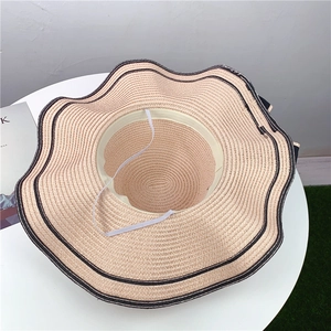 Detailed top view of beige straw sun hat with black wavy trim and elastic chin strap