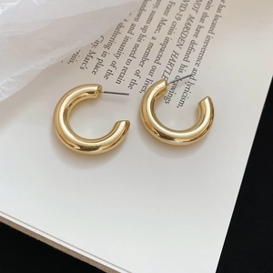 Polished gold C-shaped hoop earrings displayed on an open book with modern design