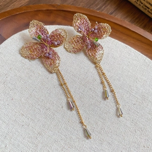 Dettaglio degli orecchini con fiori in maglia rosa e nappe su una base di lino beige
