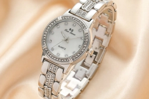 Macro shot of silver quartz watch with diamond-encrusted bezel on champagne silk