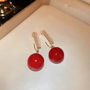 Close-up of red pearl earrings with gold alloy and zircon inlay on a beige tray