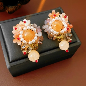 Détail de boucles d'oreilles fleuries avec perles, gemme orange et breloques en cristal