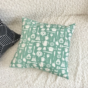 Detail of green linen pillowcase with white kitchen utensils pattern on soft white faux fur