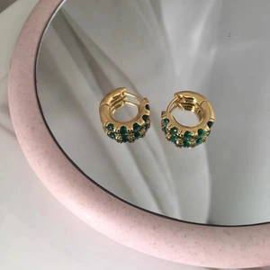 Macro detail of gold plated hoop earrings featuring double rows of sparkling green zircons