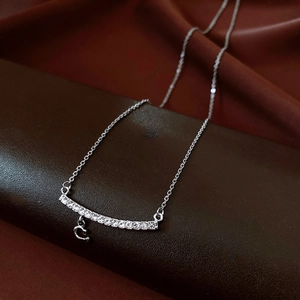 Macro shot of silver C-shaped necklace with cubic zirconia on brown leather surface