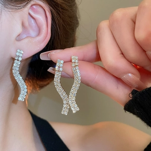 Macro detail of gold wave earrings with sparkling pavé rhinestones in long fringe style
