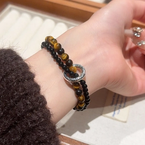 Detail of double-layer tiger eye stone and black bead bracelet on wrist with retro ring clasp