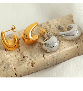 Macro shot of minimalist gold and silver teardrop earrings on a beige travertine stone base
