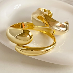 Macro shot of liquid metal style gold rings with organic folded design on white ceramic