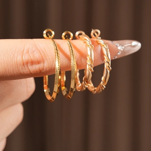 Detailed close-up of gold twist and textured hoop earrings held on fingers