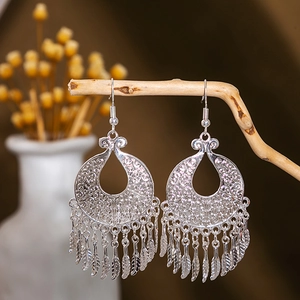 Macro detail of silver hollow leaf earrings with ethnic feather tassels on wood