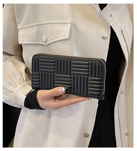 Close-up of black quilted long wallet with gold zipper held by a model in a beige coat