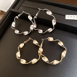 Détail de boucles d'oreilles créoles torsadées or et argent au design ondulé