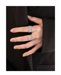 Detail showing hollow heart silver rings worn on hand against a dark blazer background