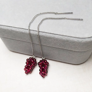 Macro shot of handmade garnet grape cluster drop earrings on a grey velvet display box