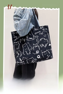 Detail view of black canvas tote bag with white cartoon cat pattern and wide shoulder strap