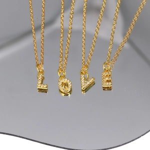 Gold letter pendant necklaces L-O-V-E with zircon stones on a reflective mirror surface
