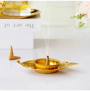 Close-up of golden leaf-shaped metal incense burner with rising smoke on a desk