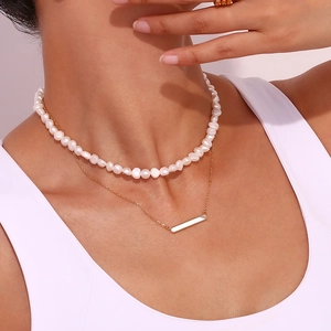 Détail du collier superposé avec perles d'eau douce blanches et pendentif barre dorée