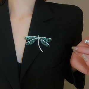 Detailweergave van libelle broche met groene strass-steentjes op een zwart jasje