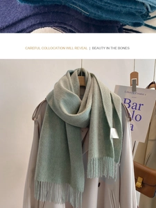 Close-up of sage green wool scarf texture with fringe details on a beige coat