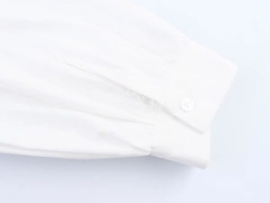 Dettaglio del polsino della camicia bianca con cuciture fini e un singolo bottone in resina