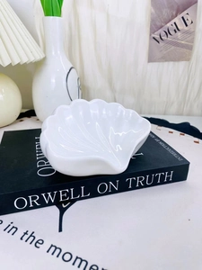 Dettaglio portasapone in ceramica bianca a forma di conchiglia su un libro nero