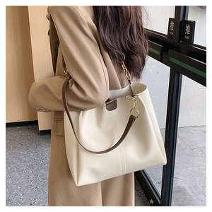 On-shoulder view of large beige tote bag with dark brown straps on khaki blazer