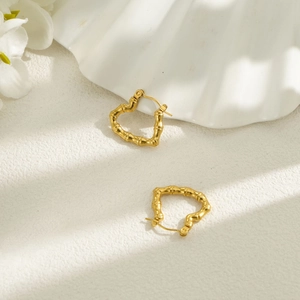 Detailed close-up of 18k gold heart-shaped bamboo textured earrings on a white shell background