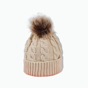 Detailed close-up of beige knit beanie featuring a premium faux fur pompom and thick texture