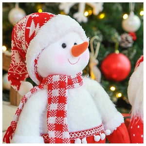 Dettaglio di un pupazzo di neve di peluche con cappello di maglia rosso e sciarpa natalizia