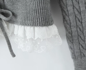 Detailed view of grey knit cardigan hem featuring double-layered white lace with bow embroidery