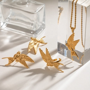 Detailed view of golden swallow necklace, earrings and ring set on glass pedestals