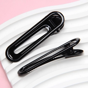Macro shot of 6cm black glossy U-shaped minimalist hair clip on a textured wave surface