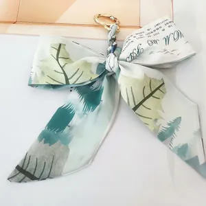 Close-up of camellia silk bow keychain with golden metal ring and forest pattern print