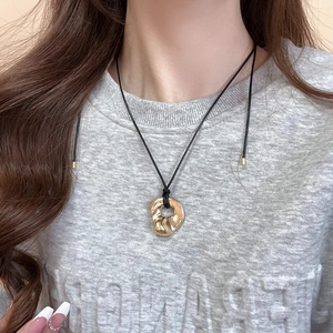 Close-up of gold irregular geometric liquid-style pendant on a black cord necklace