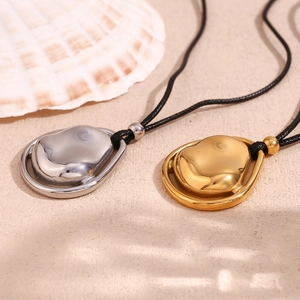 Dettaglio di pendenti organici irregolari in oro e argento su sabbia con conchiglie